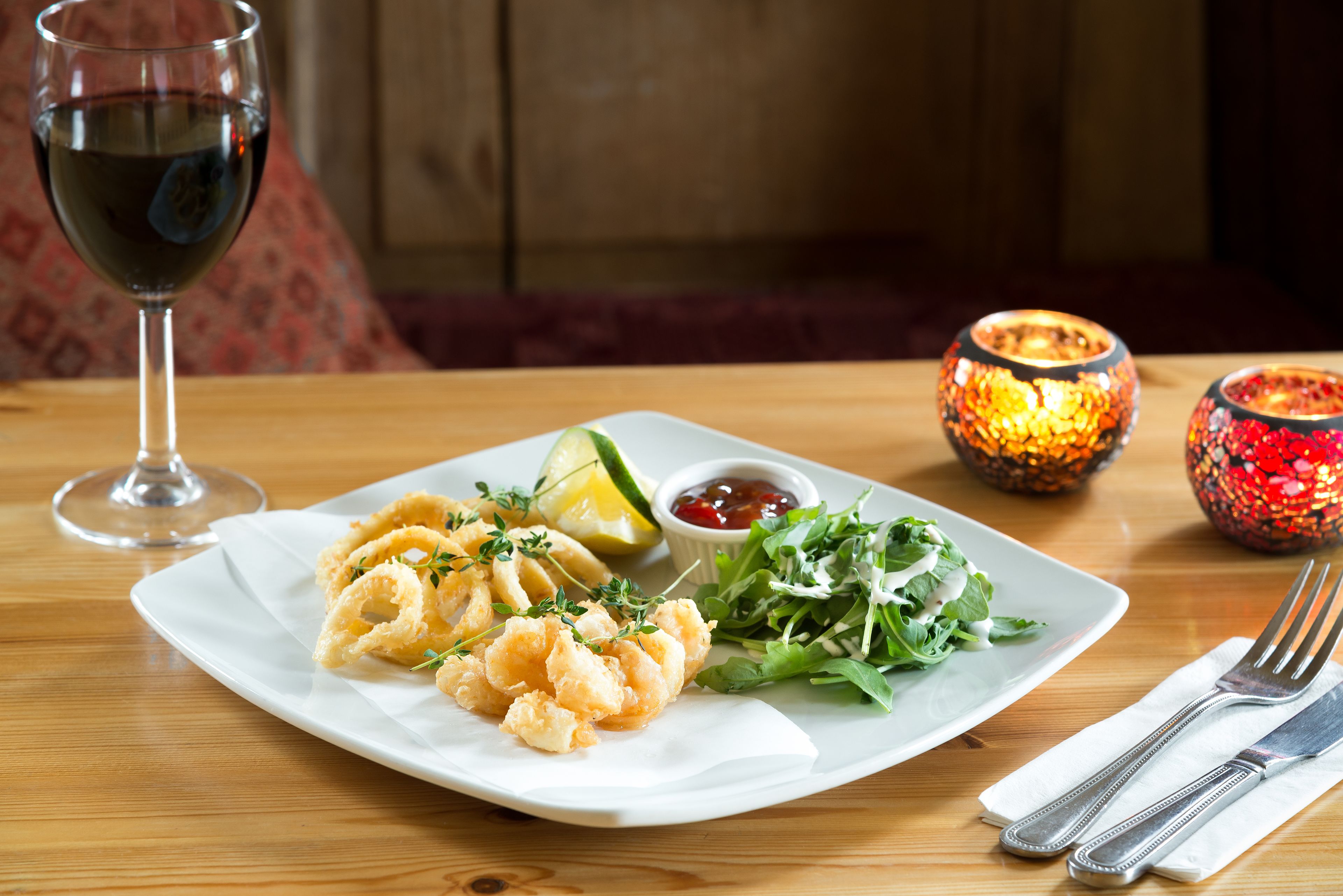 A plate of food with a glass of red wine, a salad, and a lemon wedge on a wooden table.