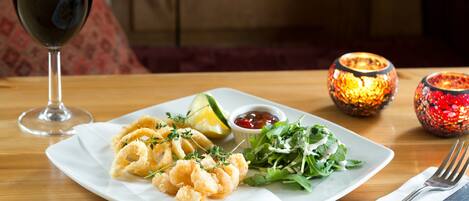 A plate of food with a glass of red wine, a salad, and a lemon wedge on a wooden table.