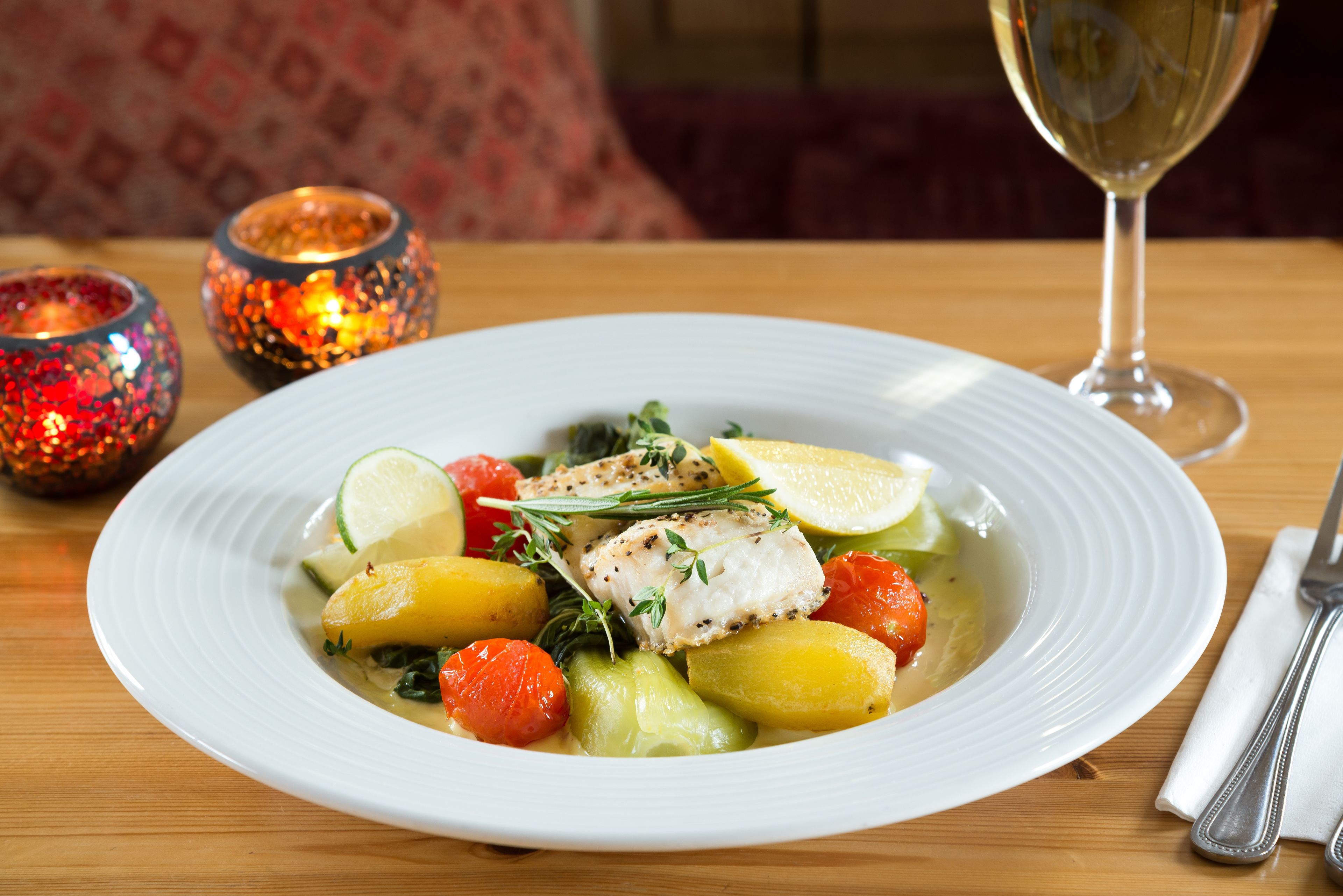 A white plate with fish, potatoes, and vegetables on a wooden table.