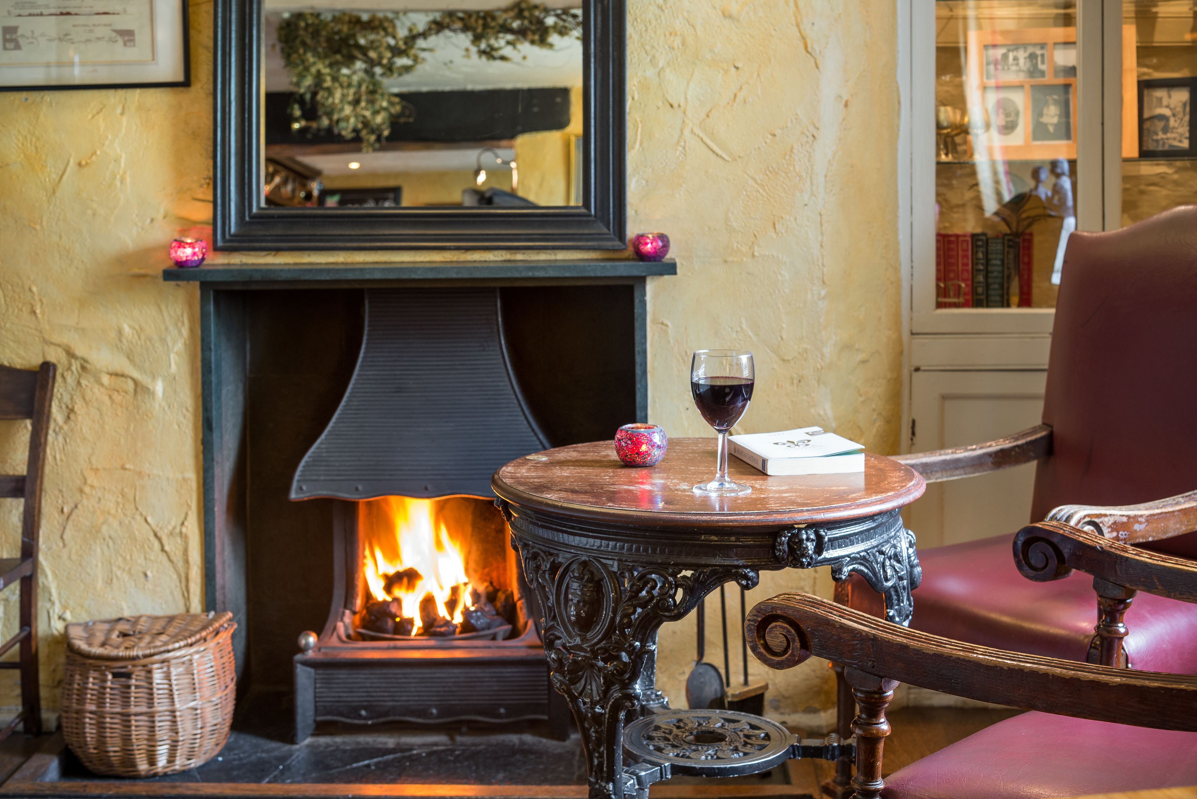 A cozy room with a fireplace, a table with a glass of wine, and a chair.