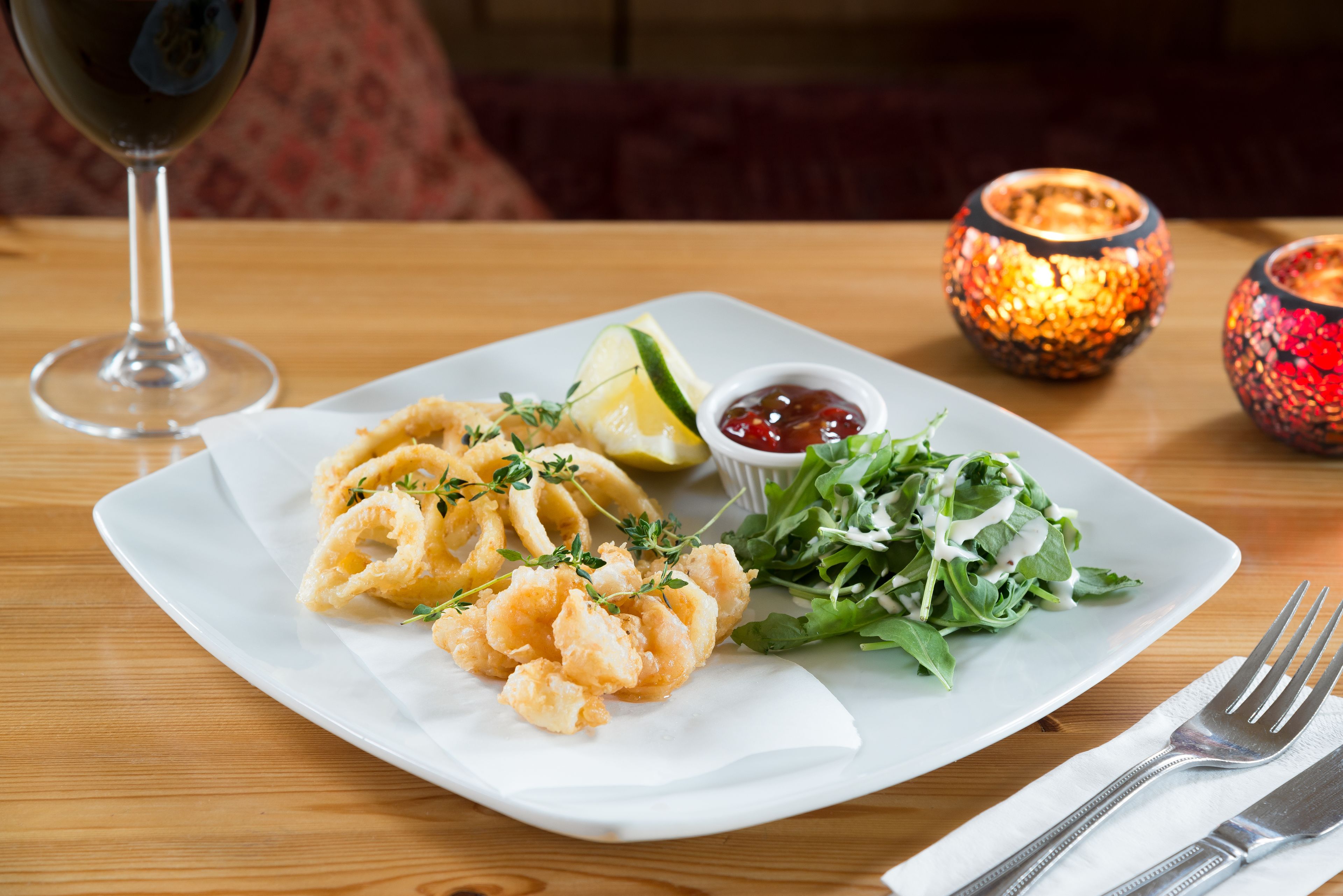 A plate of food with a glass of wine, a salad, and two decorative candles on a table.