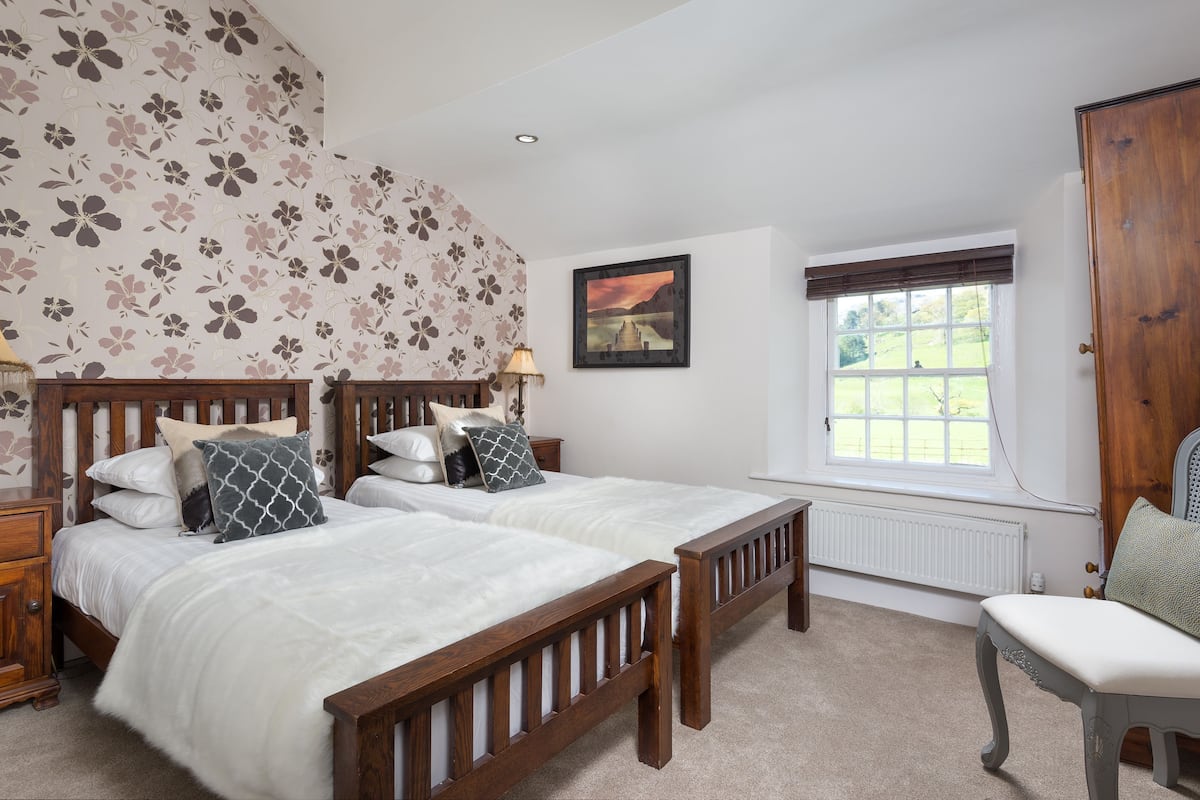 A bedroom with two wooden beds, a window with a view, a radiator, and a wooden wardrobe.