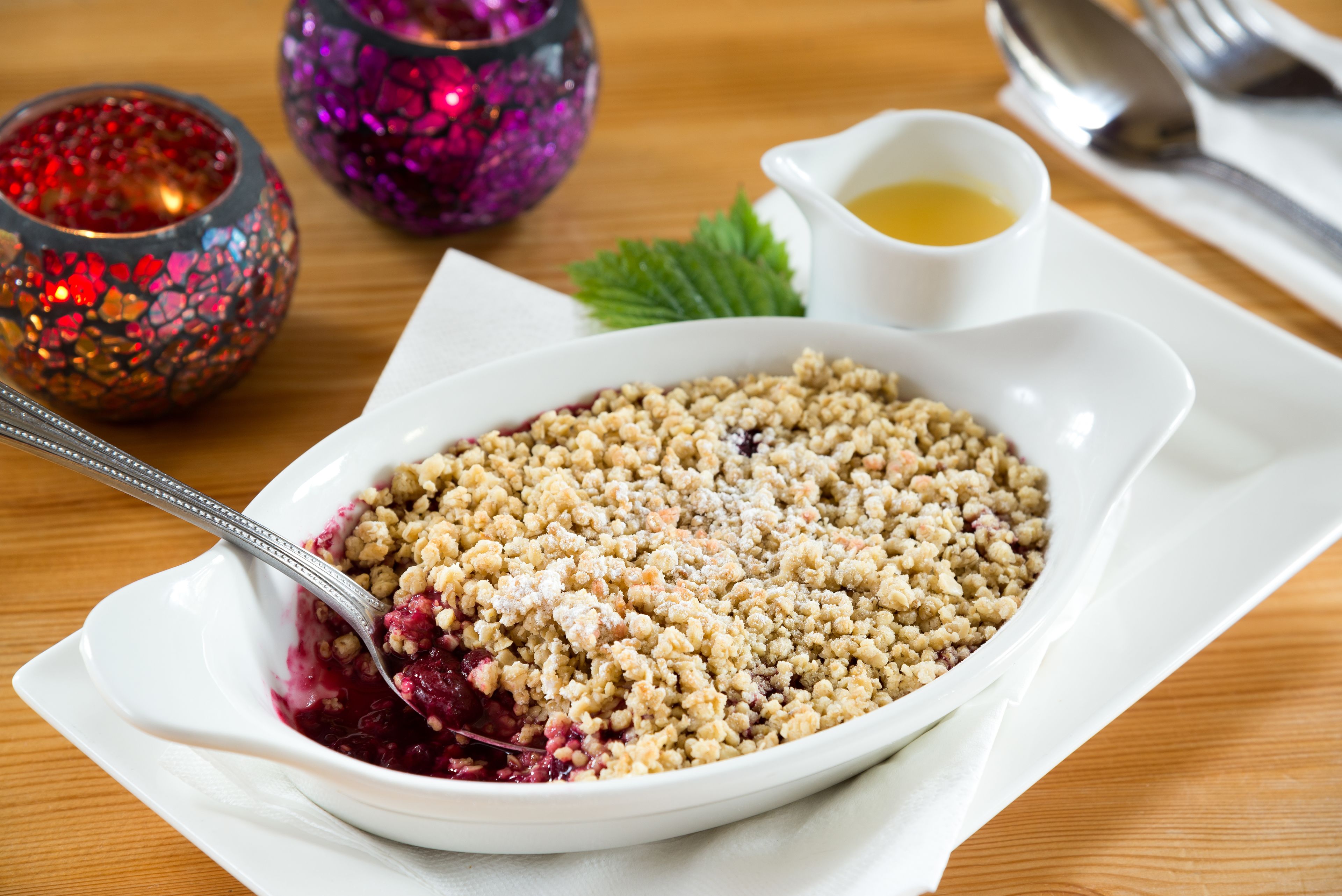 A white bowl of fruit crumble with a spoon, placed on a white plate.