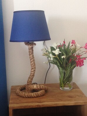 A lamp with a blue shade and a rope base on a wooden table next to a clear vase with flowers.