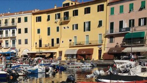A waterfront with colorful buildings, boats docked, and a clear blue sky. - Le Stanze sul Mare (Portoferraio)