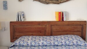 A bedroom with a wooden headboard, a patterned bedspread, and a wall-mounted decorative piece resembling a fish. - Le Stanze sul Mare (Portoferraio)