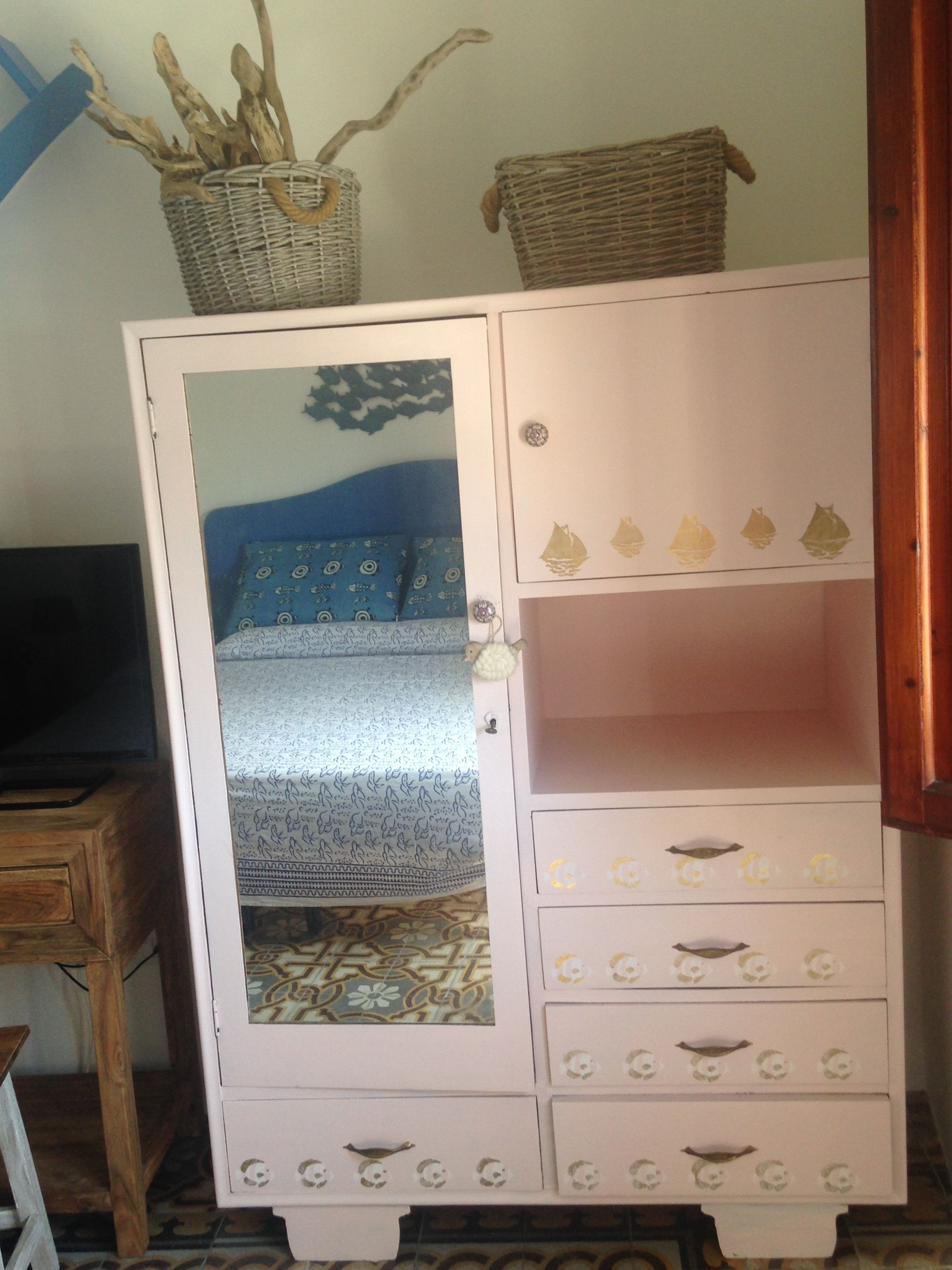 A white cabinet with multiple drawers and a glass door, decorated with small animal figures and a patterned fabric inside.