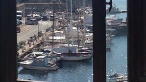 A marina with boats docked, a building with a flag, and mountains in the background. - Le Stanze sul Mare (Portoferraio)