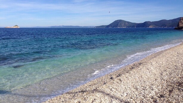A pebble beach with clear water, distant mountains, and a small island. - Le Stanze sul Mare (Portoferraio)