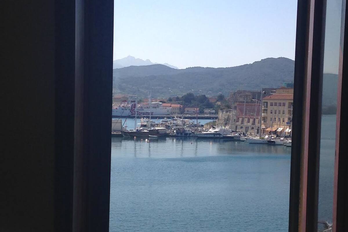 A view through a window of a harbor with boats, a large ship named 'Torremur', and buildings in the background.