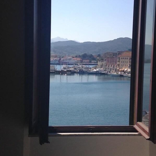 A view through a window of a harbor with boats, a large ship named 'Torremur', and buildings in the background. - Le Stanze sul Mare (Portoferraio)