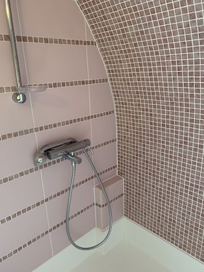 Un baño con zona de ducha, paredes de azulejos y cabezal de ducha cromado.
