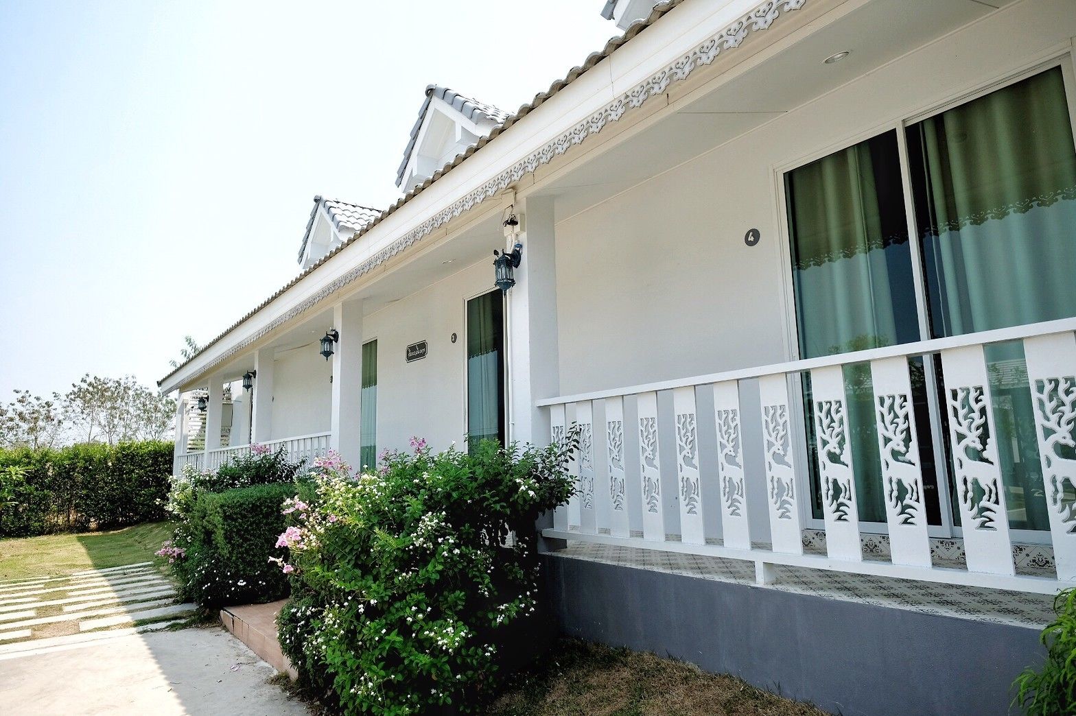A two-story building with a white facade, a covered porch, and decorative window grills.