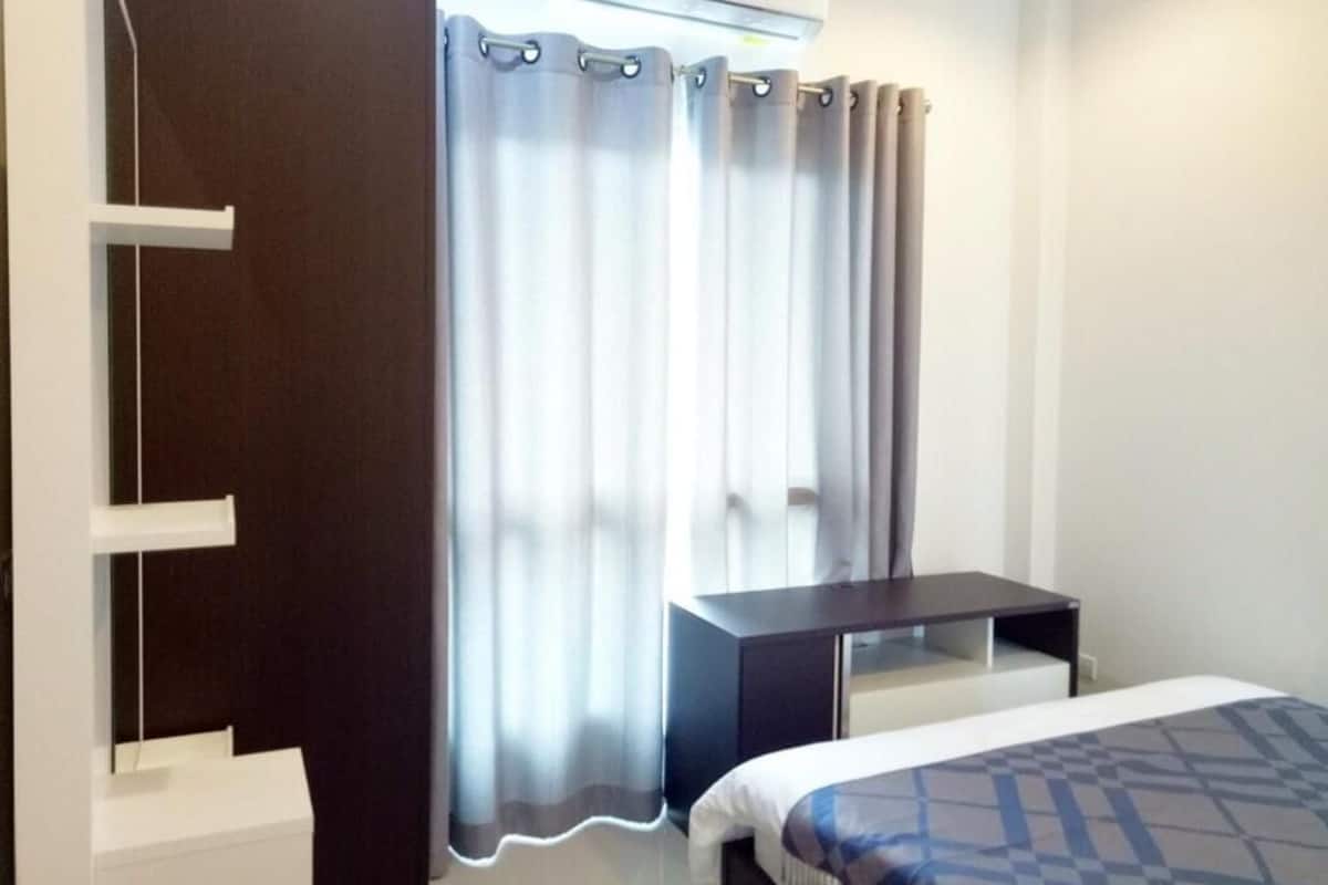 Ett hotellrum med en säng, ett skrivbord, en stol, en garderob och ett fönster med gardiner.