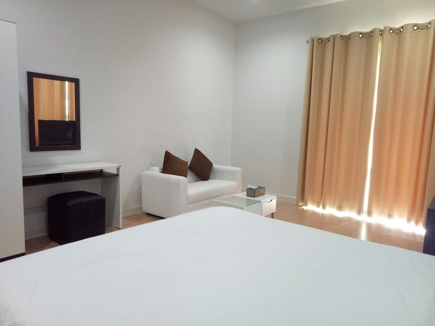 A hotel room with a bed, a white sofa, a small table, a desk, and a mirror.