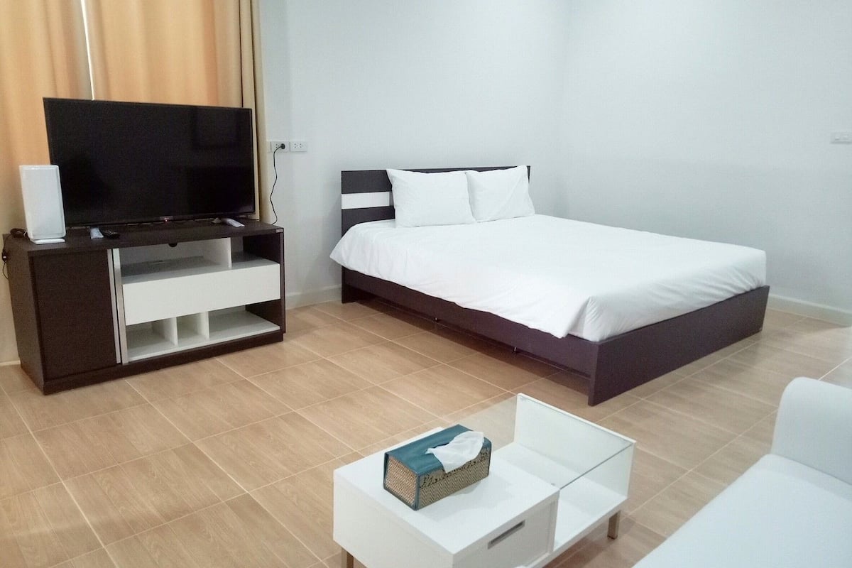 Ett modernt hotellrum med en säng, en tv på ett stativ, en vit soffa och ett soffbord.