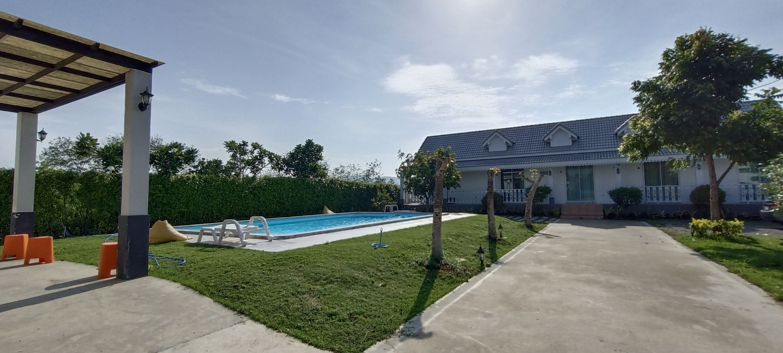 Un jardin avec une piscine, un patio couvert et une maison avec un toit en tuiles.
