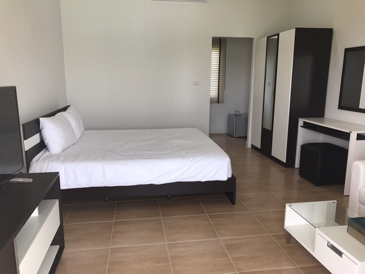 A modern hotel room with a large bed, a desk, a TV, and a wardrobe.