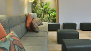 A modern living room with a sofa, ottomans, and a potted plant. - Spot Apartments Trindade (Porto)