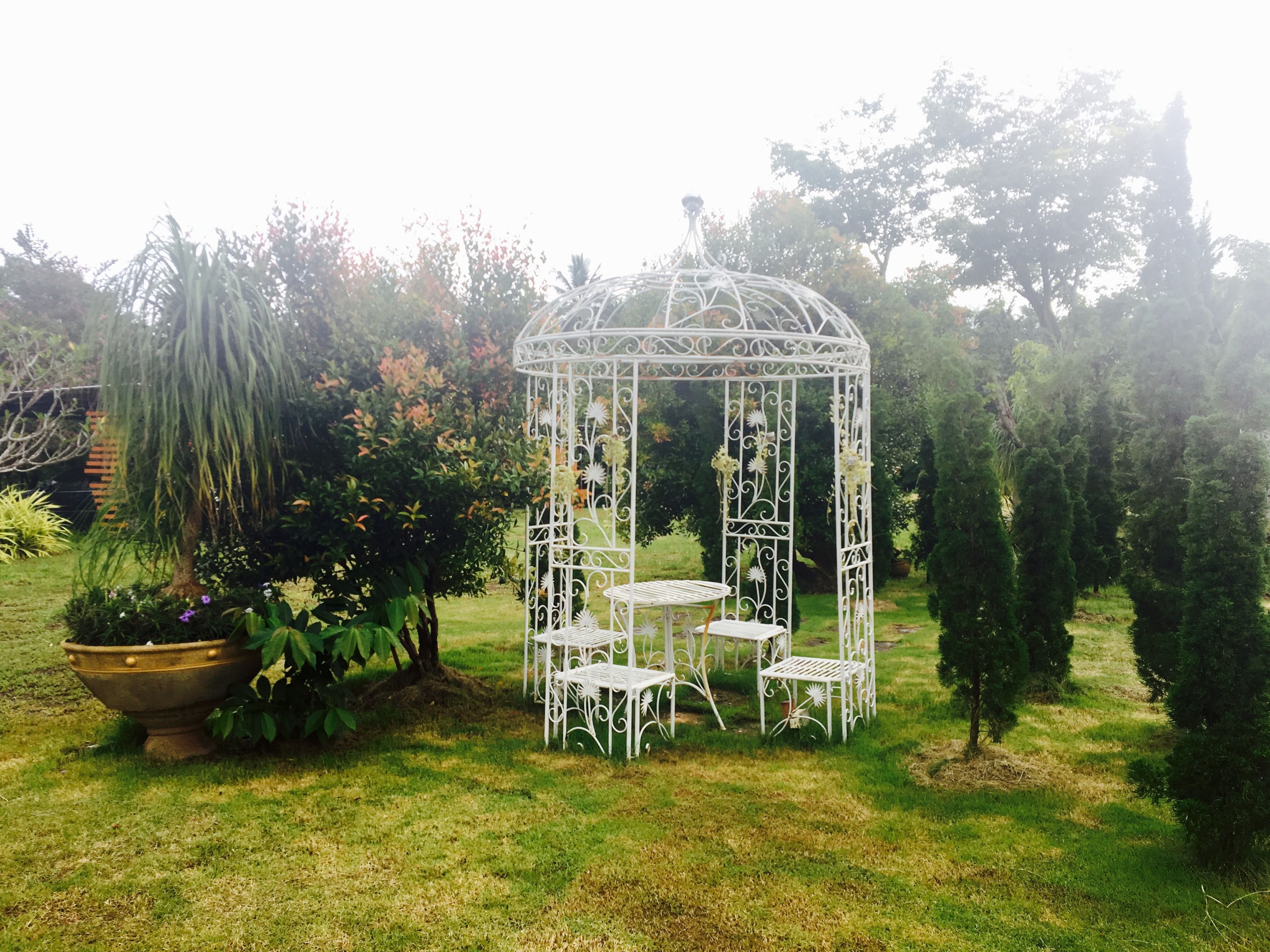 Un pabellón metálico blanco con una mesa y sillas en un jardín.