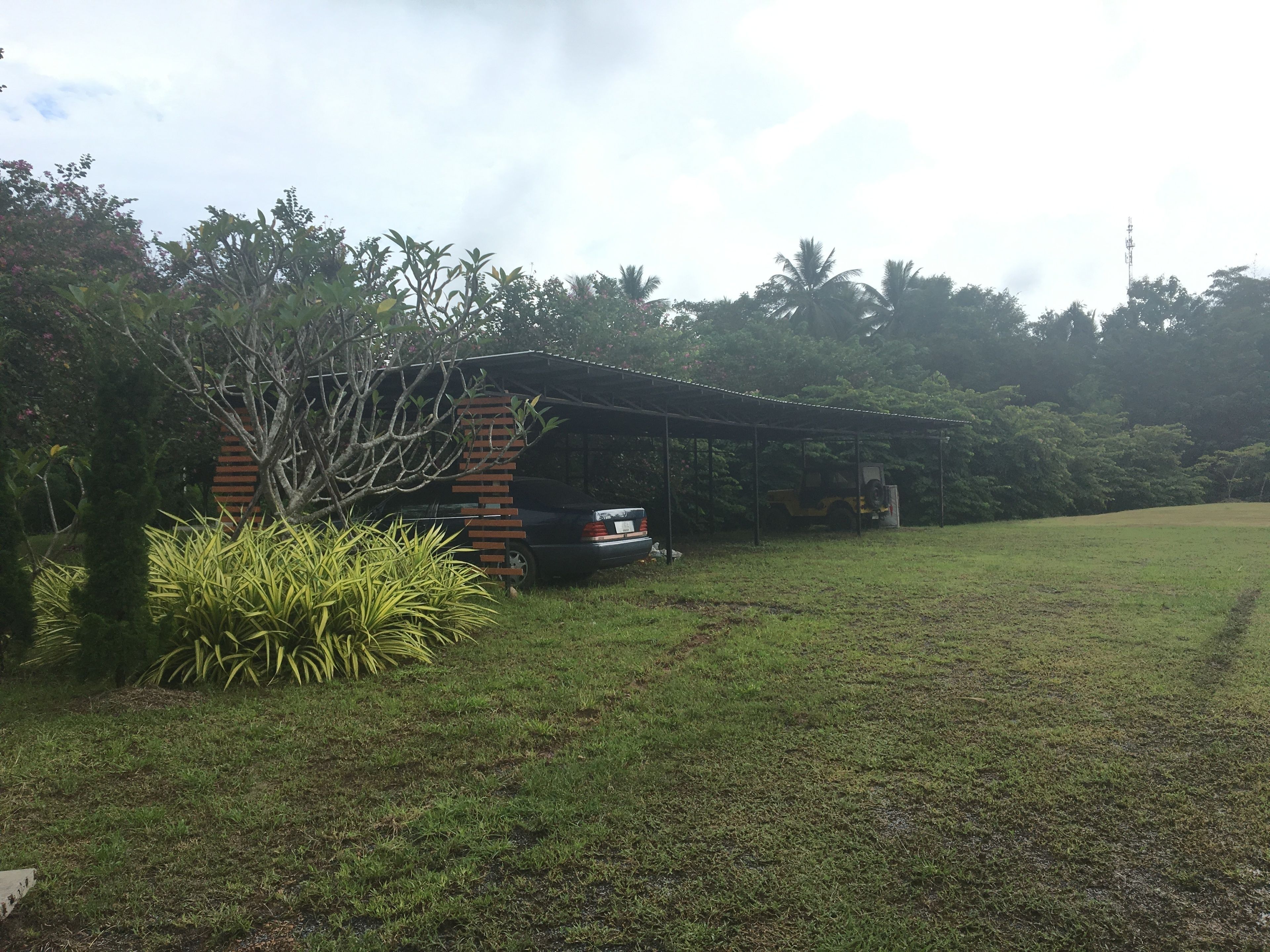 A small brick building with a covered porch, surrounded by lush greenery and a grassy field.
