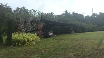 A small brick building with a covered porch, surrounded by lush greenery and a grassy field.