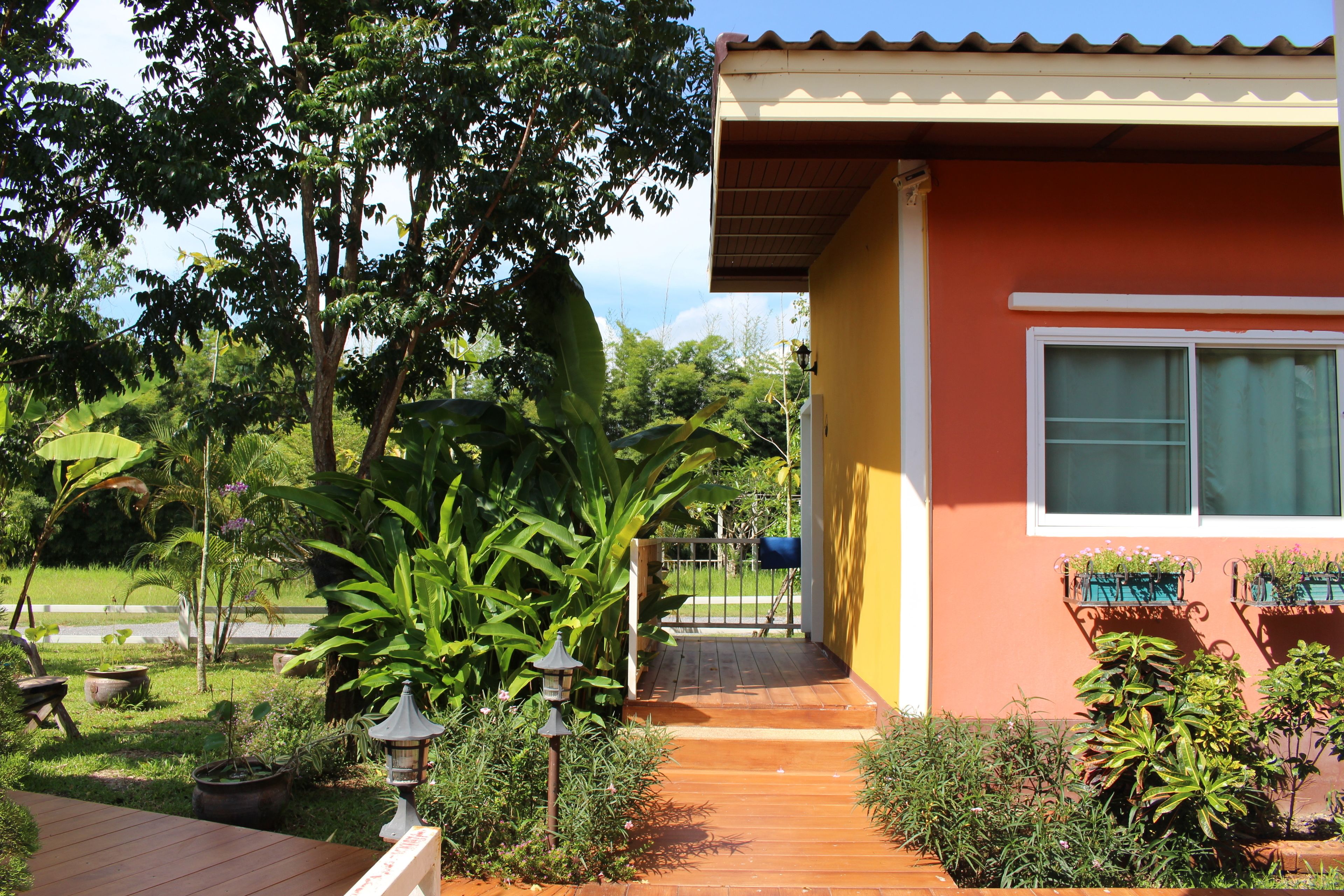 Una casa con terraza de madera, un jardín con diversas plantas y un buzón.
