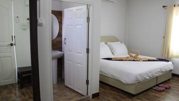 Un dormitorio con cama, mesita de noche, espejo, baño con lavabo y puerta que da a otra habitación.