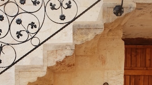 A stone wall with a rustic wooden door, a metal railing with floral designs, and a stone sink with a wooden shelf above it. - Ali Bey Konagi (Gaziantep)