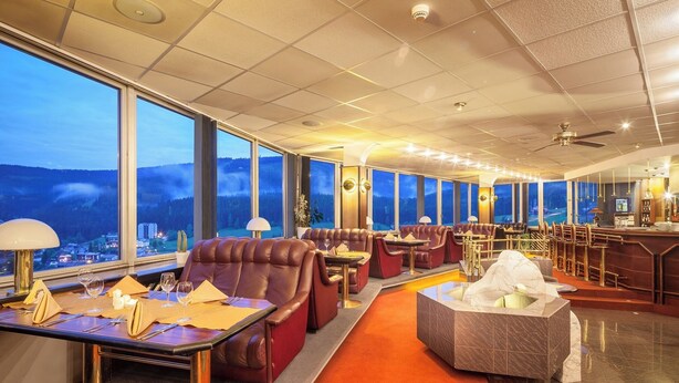 Un restaurante de techos altos con asientos de cuero, una zona de bar y grandes ventanales que ofrecen vistas a la montaña.