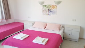 Un dormitorio con dos camas, cada una con ropa de cama rosa y toallas blancas. Hay dos mesitas de noche y un aplique en la pared.