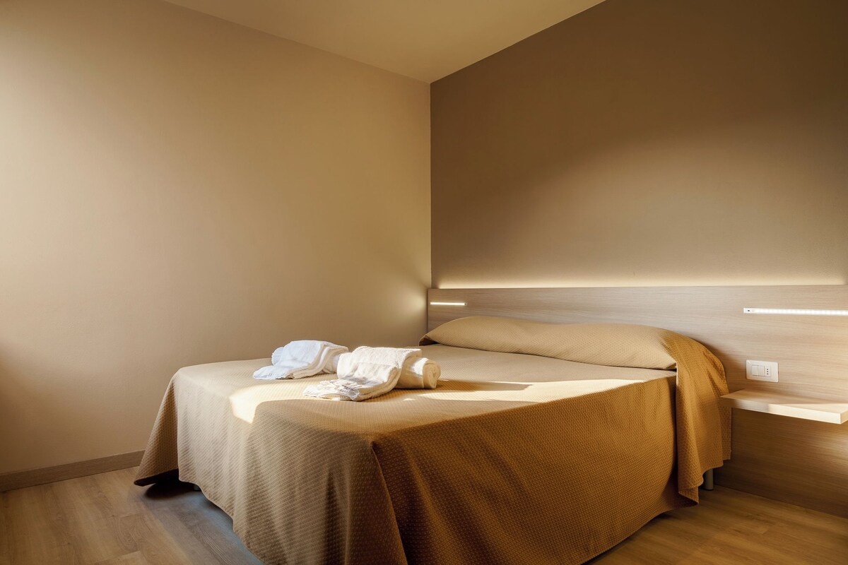 Una habitación de hotel moderna con cama, mesita de noche y lámpara de pared.