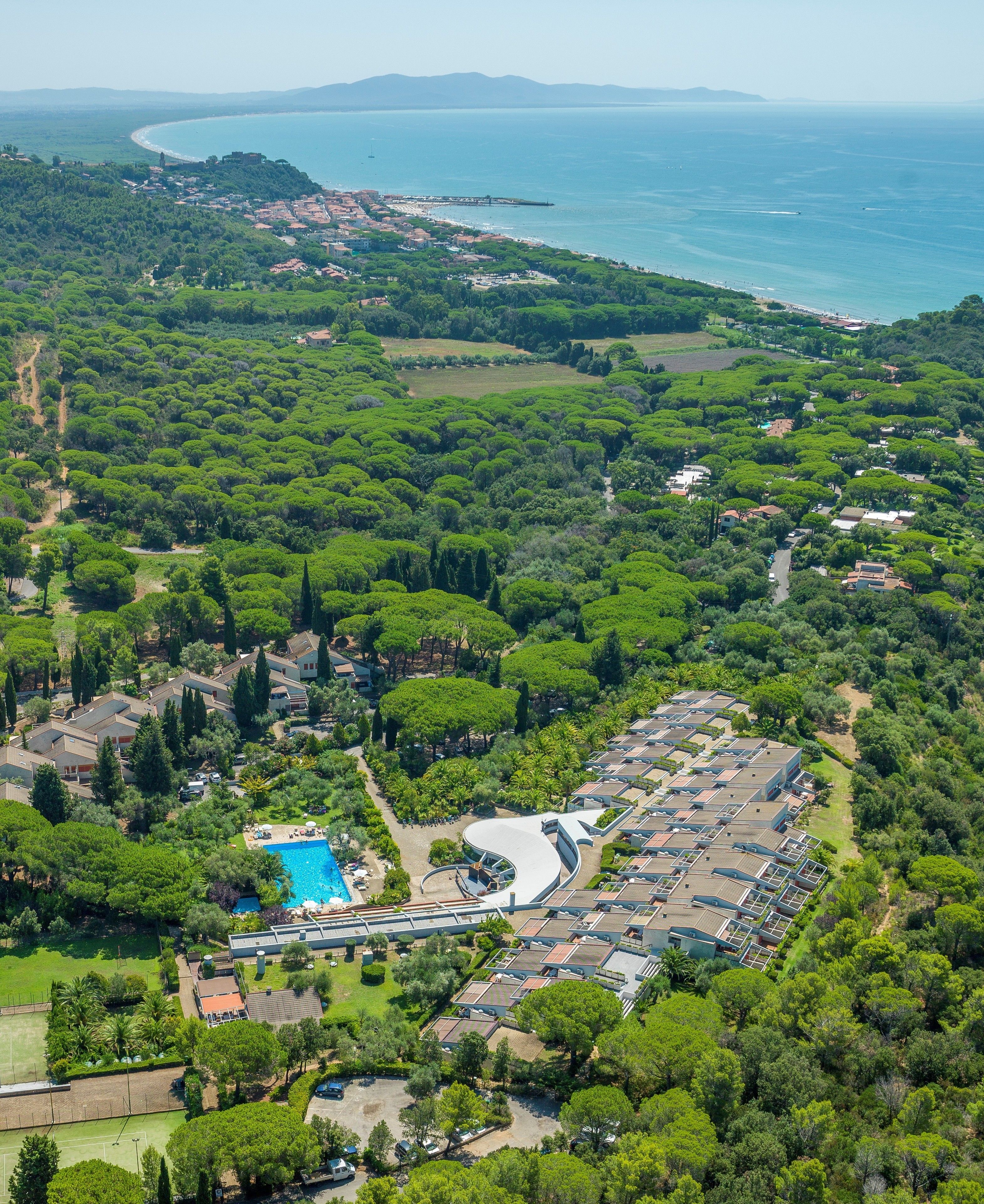 An aerial view of a coastal area with a large pool, dense greenery, and a mix of residential and commercial buildings.