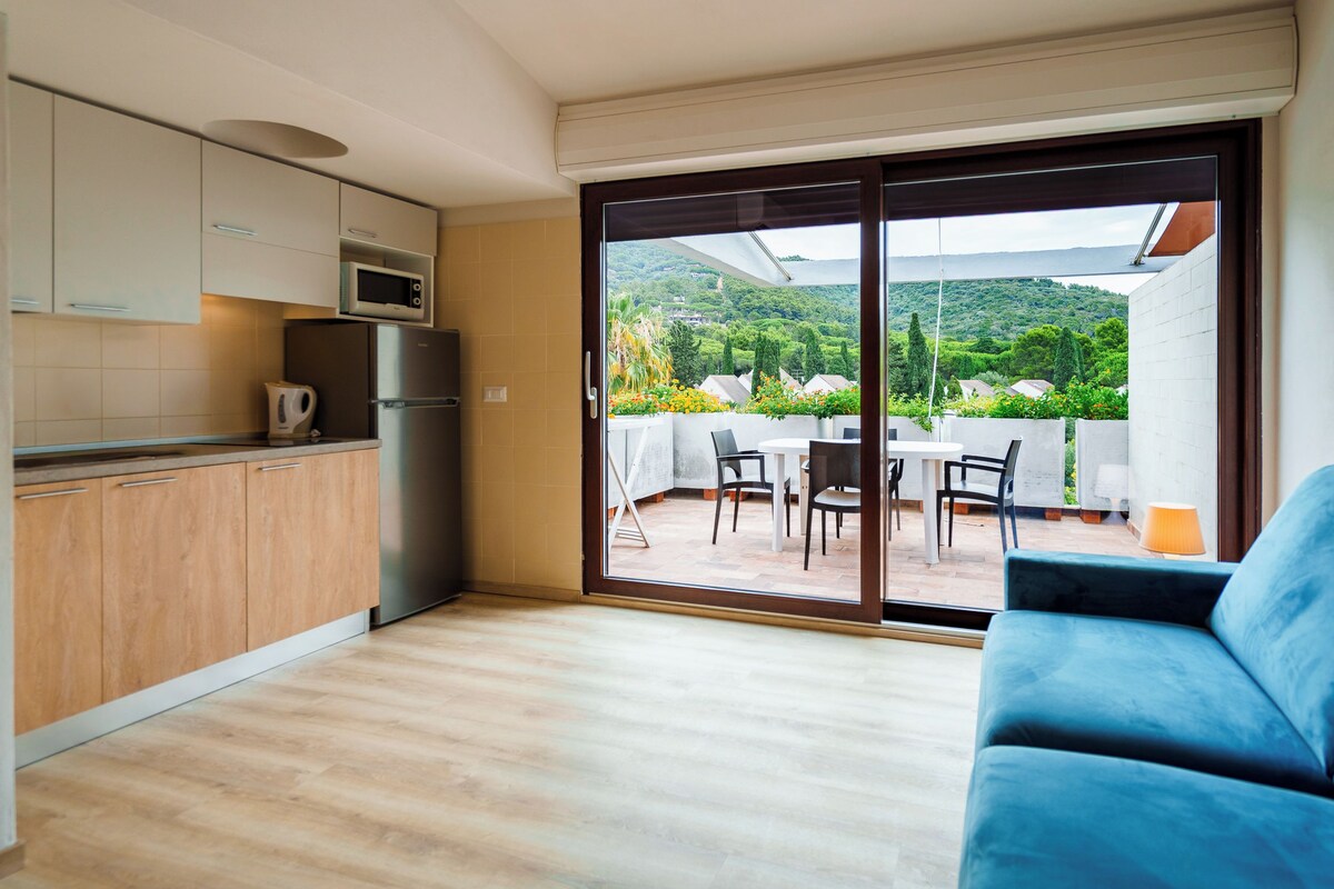 Una cocina moderna con microondas, refrigerador y hervidor, que da a un área de comedor con una mesa y sillas, y un sofá azul.