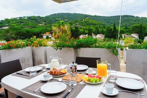 Mesa de comedor al aire libre dispuesta con alimentos para el desayuno, vista a un paisaje verde exuberante y cielo despejado.