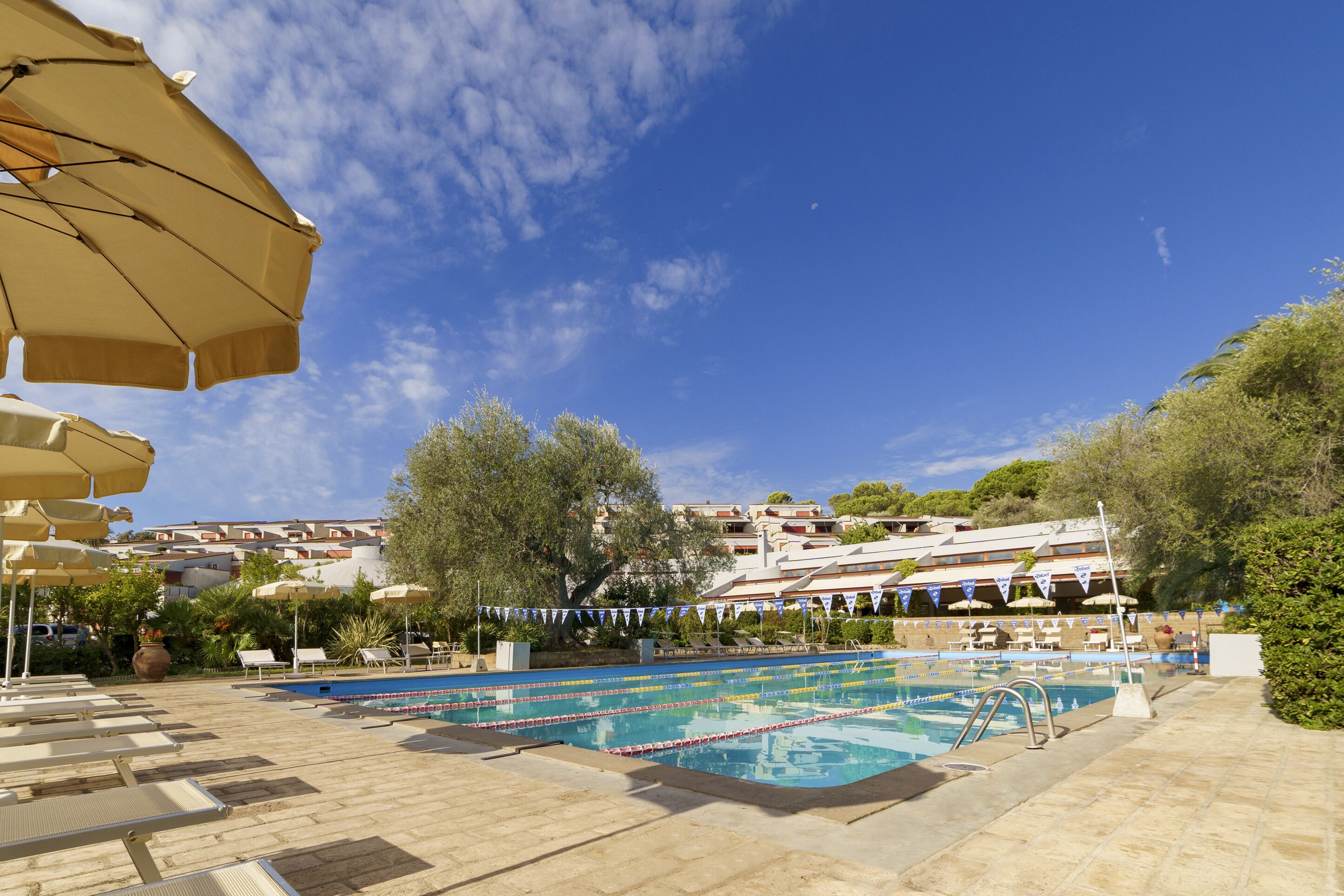 A swimming pool with lounge chairs and umbrellas, surrounded by trees and buildings.