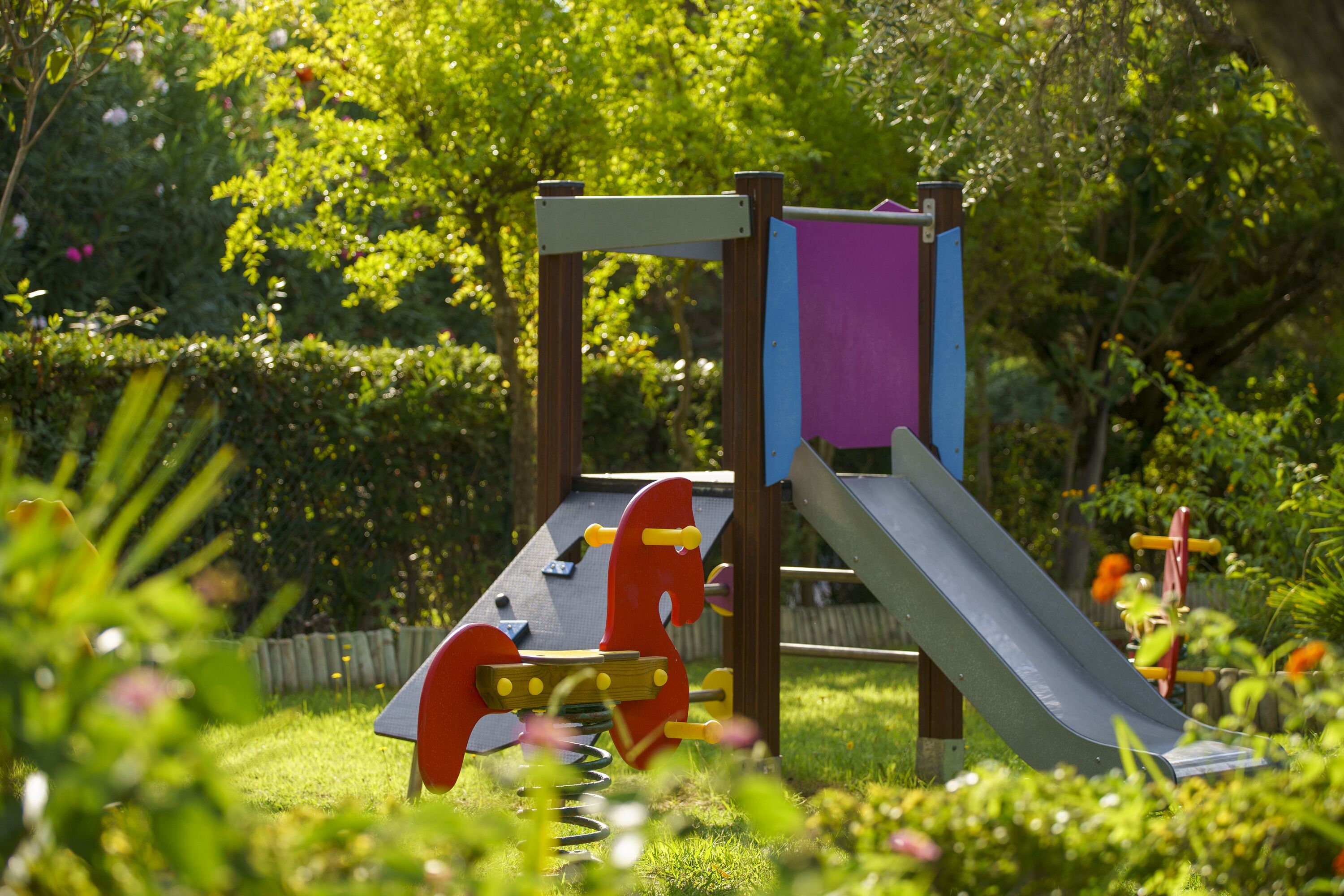 A playground with a slide and a climbing structure in a garden setting.