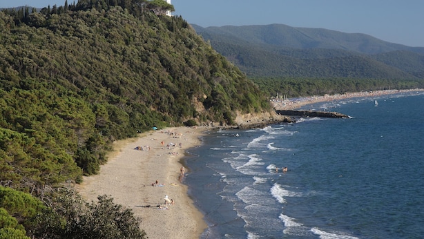 Ein Küstenstrand mit einer Hügelkuppe und einem Gebäude darauf.