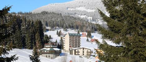 A snow-covered mountain with a ski resort, including a multi-story hotel with balconies and a ski lift in the background.