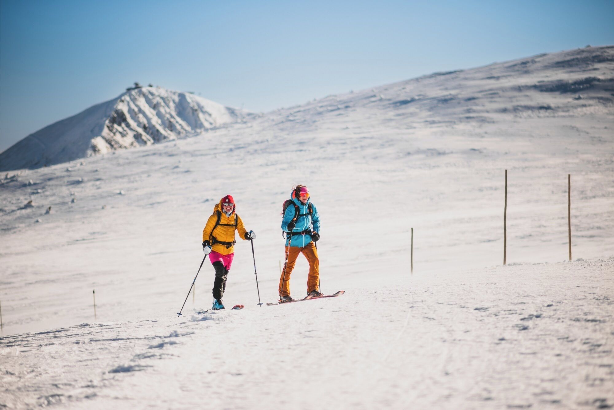 Two skiers on a snowy slope with a mountain in the background.