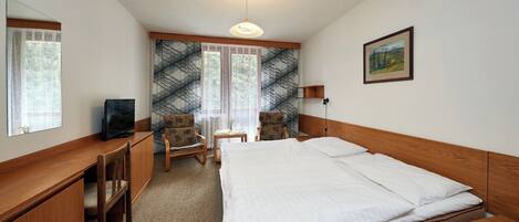Una habitación de hotel con una cama, un escritorio, una silla, un televisor y un cuadro en la pared.