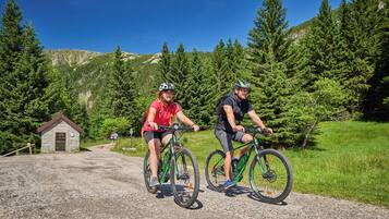 Two cyclists on a gravel path with a small stone building in the background.