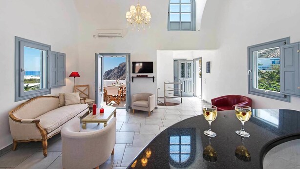 A spacious living room with a sofa, chairs, a dining area, and a bar with glasses. - Felicity Villas Santorini Luxury House (Santorini)