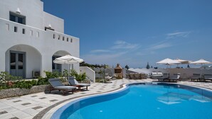 A poolside area with lounge chairs and umbrellas, a clear blue sky, and a white building with arched windows. - Felicity Villas Santorini Luxury House (Santorini)
