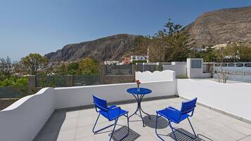 Una terraza con sillas azules y una mesa, con vista a un paisaje montañoso.