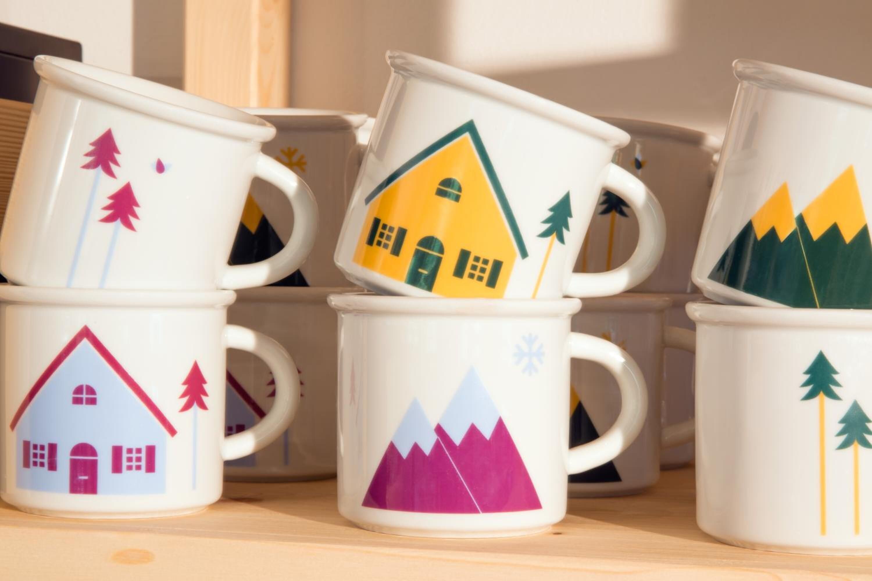 Un conjunto de tazas blancas con diversos diseños coloridos, que incluyen casas y montañas.