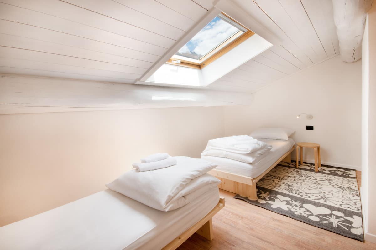 A room with two single beds, a skylight, wooden flooring, and a patterned rug.