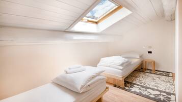 Ein Zimmer mit zwei Einzelbetten, einem Oberlicht, Holzboden und einem gemusterten Teppich.