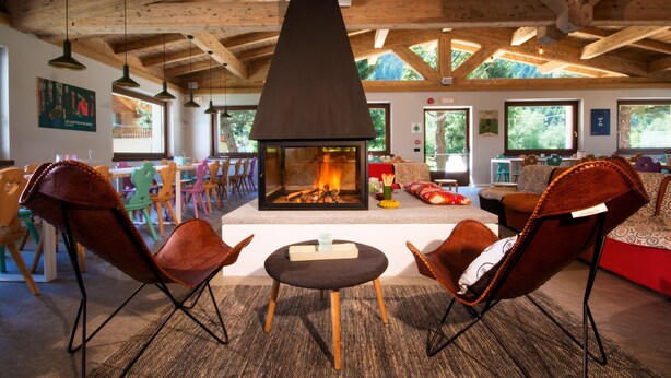 Un salon chaleureux avec une cheminée, des poutres en bois et des fauteuils aux couleurs vives.