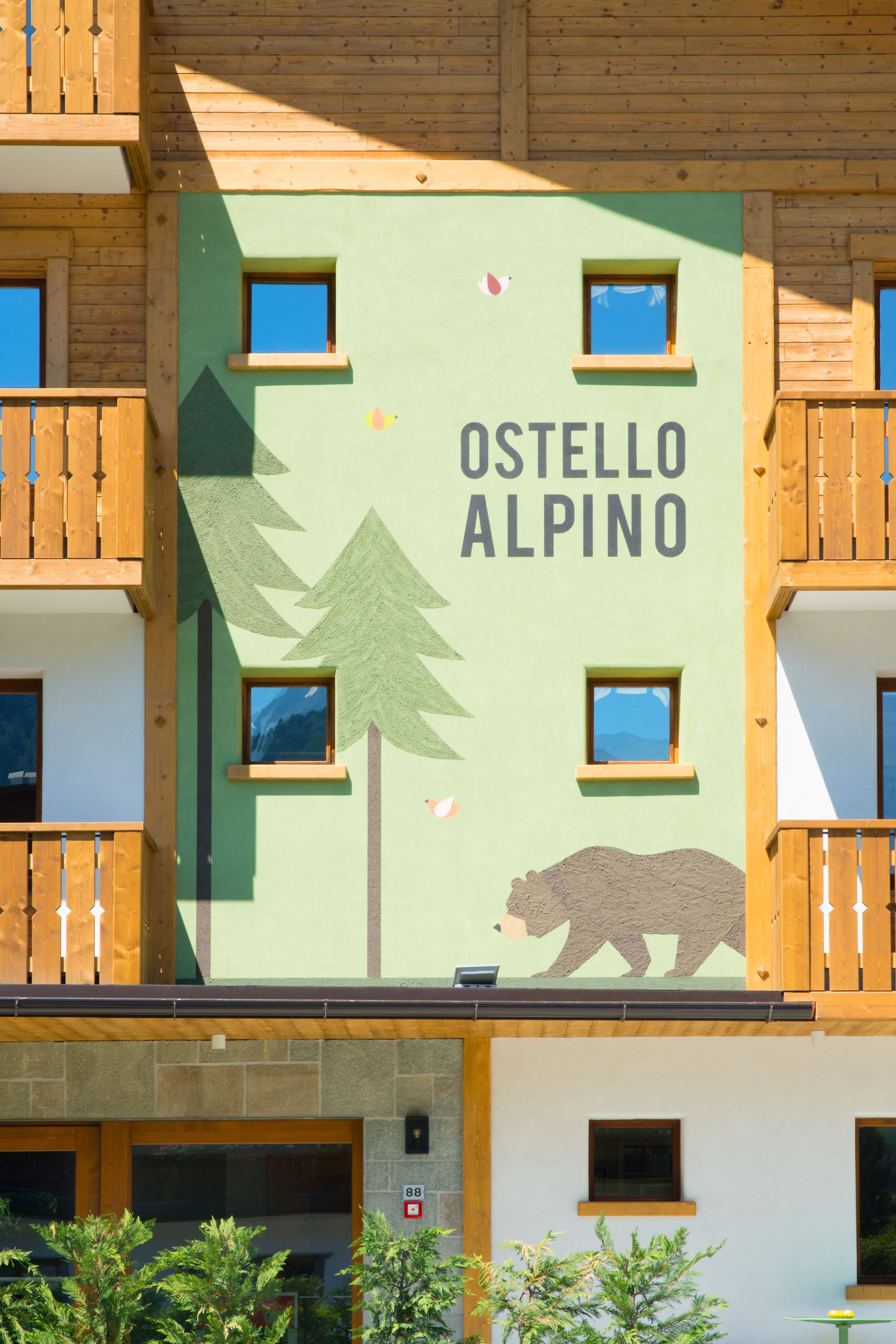 Ein Gebäude mit der Aufschrift "Ostello Alpino" und einer Bär-Grafik an der Fassade.